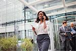 Businesswoman talking on cell phone walking out of office building