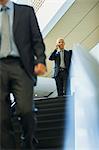 Businessman talking on cell phone at top of escalator in office