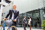 Businessman walking bicycle outside of office building