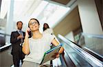 Businesswoman talking on cell phone while going down escalator