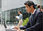 Businessman working on laptop outside of office building