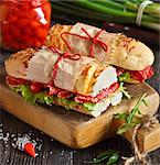 Salami sandwiches with lettuce and sweety drop peppers on an old wooden board.