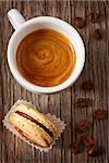 Cup of coffee with chocolate macaron on wooden background with copy space for text.