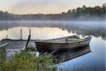 A dirty boat is parked by a wooden pier on a calm lake. It is dawn and soon the sun will be rising.