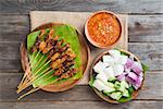 Overhead view Malaysian chicken satay with delicious peanut sauce, ketupat, onion and cucumber on wooden dining table, one of famous local dishes.