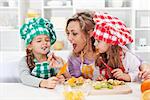 Woman and little girls preparing a fruit salad, tasting the ingredients - happy family moments