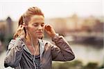 Portrait of fitness young woman wearing earphones in city in the evening