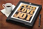 peace, love and joy word abstract - a collage of text in letterpress wood type on a digital tablet with a cup of coffee