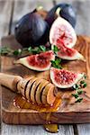 Ripe purple figs, thyme and homey on olive board. Selective focus.