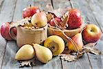 Ripe pears and apples with dry fall leaves on wooden background. Selective focus.