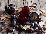 Homemade plum juice with fresh prunes and fall leaves on wooden background