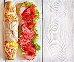 Salami sandwich with lettuce and sweety drop peppers on a white wooden board with place for text.