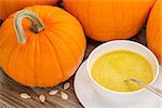 pumpkin cream soup - a bowl surrounded by pumpkins on a rustic wooden table