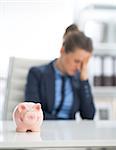 Closeup on piggy bank and frustrated business woman in background