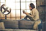 Happy young woman sitting in loft apartment and using tablet pc