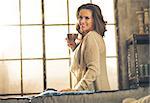 Happy young woman enjoying cup of coffee in loft apartment