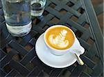 Close-up of cappuccino with latte art in white cup and saucer with water bottle and glass on patio table, Canada