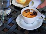 Cream being poured into coffee in white cup and saucer on outdoor, patio table, Canada