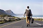 Rear view of young man with guitar case walking on coastal road, Cape Town, Western Cape, South Africa