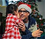 Daughter whispering to father in santa hat at christmas