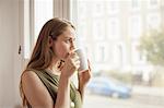 Young woman drinking coffee and gazing through sitting room window