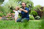 Father holding baby daughters hands whilst toddling in garden