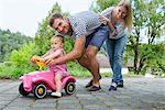 Mid adult couple pushing baby daughter on toy car  in garden