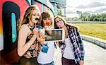 Friends taking selfie wearing fake lips and moustache, mural in background