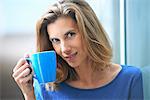 Portrait of mid adult businesswoman leaning against glass wall drinking coffee