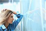 Mid adult businesswoman leaning against glass wall in office with hand in hair