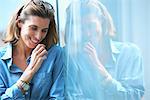 Candid shot of mid adult businesswoman leaning against glass wall in office