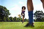 Young woman kicking soccer ball toward boyfriend in park