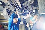 Three college students looking up at car in garage workshop