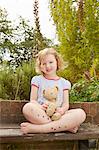 Portrait of girl on garden seat with teddy bear and star stickers on legs