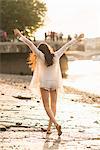 Young woman walking along river, arms out