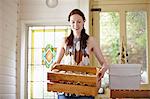 Female beekeeper in kitchen carrying a crate of honey jars from beehive