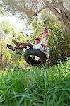 Two girls sitting and standing on tree swing in garden