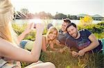 Young woman taking smartphone photograph of friends on riverbank