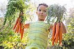 Portrait of boy in garden holding up bunches of carrots