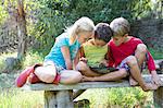 Three children sitting on garden seat looking down at digital tablet