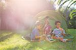 Three children eating ice lollies in garden tent