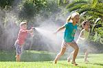 Three children in garden chasing each other with water sprinkler