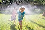 Boy running after girl in garden with water sprinkler