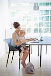 Mid adult woman and toddler daughter typing on laptop