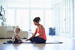 Mid adult mother and toddler daughter practicing yoga in living room