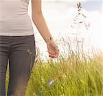 Young woman running hand through long grass in meadow under bright sunshine, close up