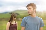 Young couple standing apart and looking away in rural landscape under bright sunny sky