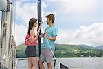 Young couple standing on bow of yacht sailing on lake under bright sunlight