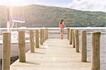 Young woman standing on jetty looking over lake on sunny day