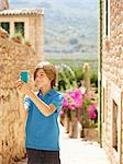 Boy taking selfie on smartphone on village street, Majorca, Spain